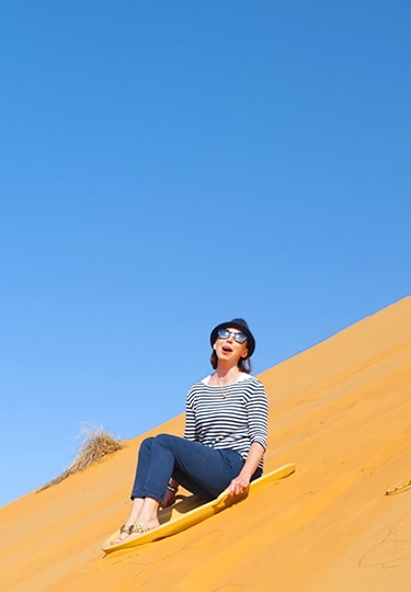 Woman on holiday and enjoying herself on a surfboard while sliding down the sand slope
